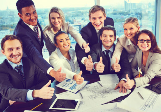 Group of business partners showing thumbs up while sitting at workplace in office